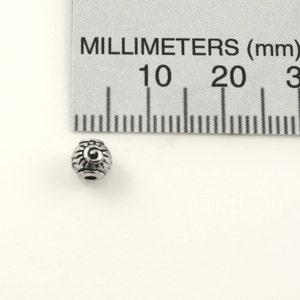 Puede incluir: Una cuenta de metal plateado con un dise&ntilde;o decorativo. La cuenta mide aproximadamente 1 cm de di&aacute;metro.