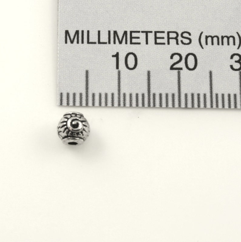 Puede incluir: Una cuenta de metal plateado con un dise&ntilde;o decorativo. La cuenta mide aproximadamente 1 cm de di&aacute;metro.