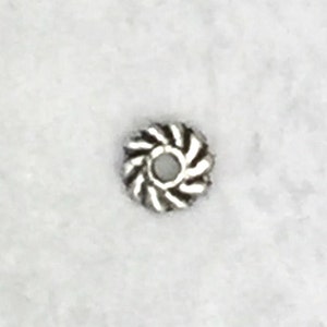 May include: A silver metal bead with a swirl design. The bead has a small hole in the center for stringing.