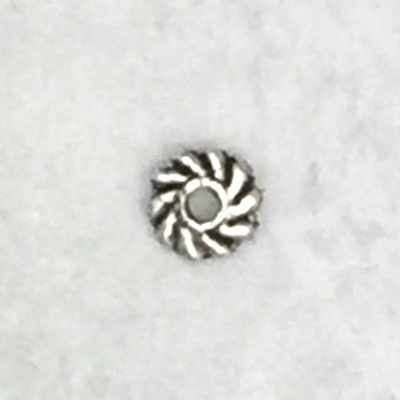 May include: A silver metal bead with a swirl design. The bead has a small hole in the center for stringing.