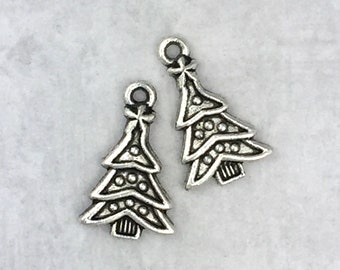 May include: Two silver-colored Christmas tree charms. Each charm has a loop at the top for hanging, a bow, and three layers of branches with small dot details. The bottom of the tree has a textured design.