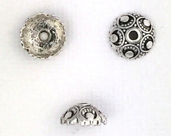 May include: Three silver metal bead caps with decorative designs. Two caps have a circular design with a raised center and the third cap has a smooth, flat surface.