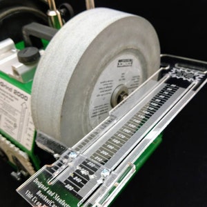 Könnte beinhalten: Nahaufnahme eines grünen SuperGrind 2000 Schleifsystems mit einer grauen Schleifscheibe und einem transparenten Winkelmesser aus Kunststoff. Der Winkelmesser ist in Schritten von 10 Grad von 60 bis 250 Grad markiert.