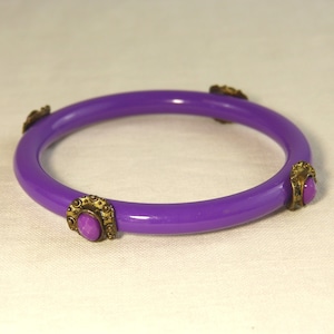 Peut inclure: Bracelet rigide violet avec quatre accents dorés, chacun orné d'une pierre précieuse violette.