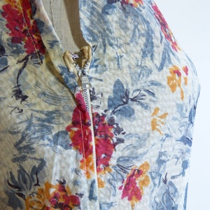 May include: A close-up of a vintage dress with a floral print in shades of blue, red, and yellow. The dress has a zip fastening and a sheer fabric.