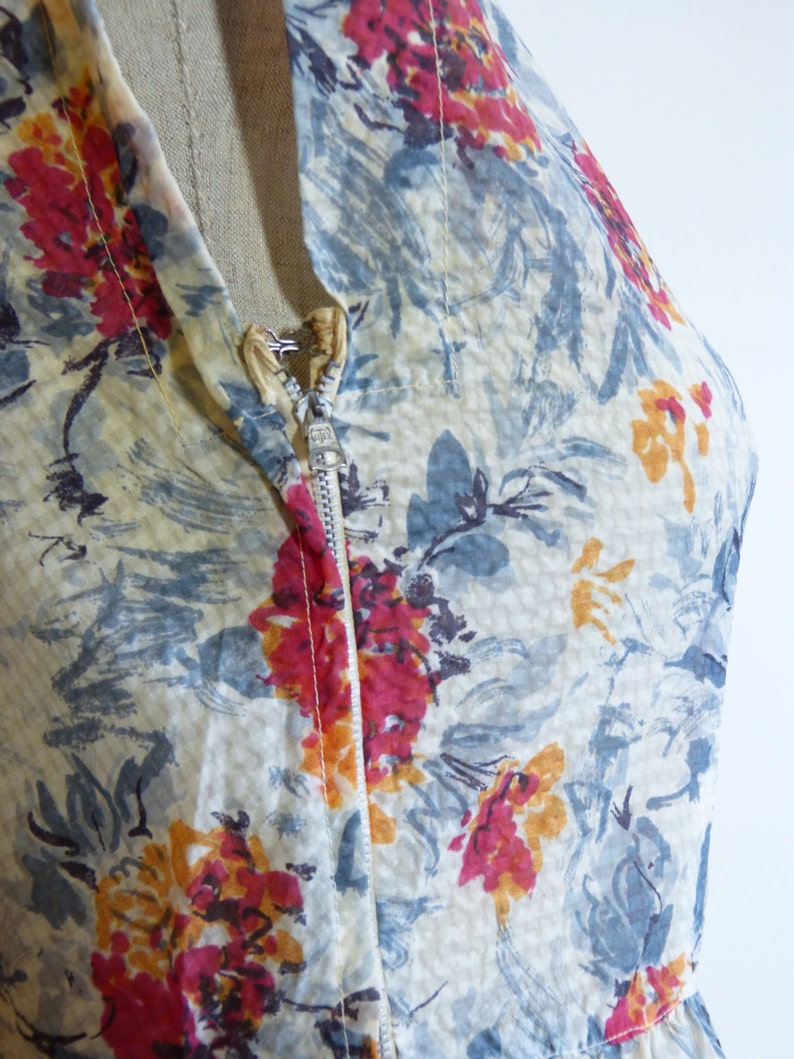 May include: A close-up of a vintage dress with a floral print in shades of blue, red, and yellow. The dress has a zip fastening and a sheer fabric.