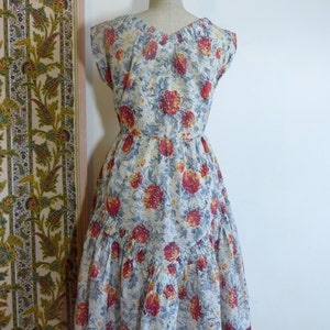 May include: A vintage floral dress with a white background and red, orange, and blue flowers. The dress has a v-neckline, cap sleeves, and a tiered skirt.