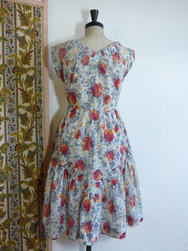 May include: A vintage floral dress with a white background and red, orange, and blue flowers. The dress has a v-neckline, cap sleeves, and a tiered skirt.
