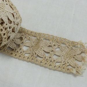 May include: A roll of beige lace with a floral design. The lace is made of a woven material and has a delicate, openwork pattern. The edge of the lace is fringed. The lace is likely used for sewing, crafting, or adding a decorative touch to garments.