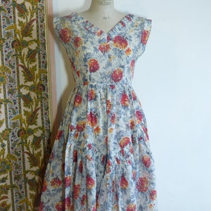 May include: A vintage sleeveless dress with a V-neckline and a floral print in shades of red, yellow, and blue on a white background. The dress has a tiered skirt and a fitted bodice.