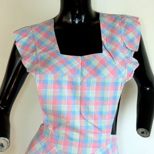 May include: A pink, blue, and green plaid apron with ruffled sleeves.