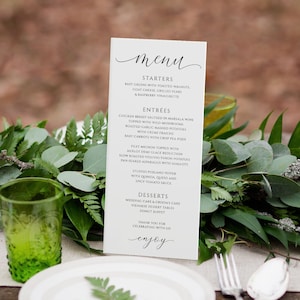 May include: A wedding menu card with a green and white color scheme. The menu lists starters, entrees, desserts, and a thank you message. The card is surrounded by greenery.