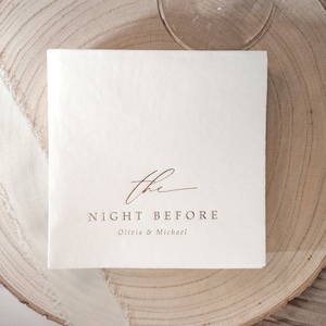 May include: White square napkin with the text "the NIGHT BEFORE Olivia & Michael" printed in gold.