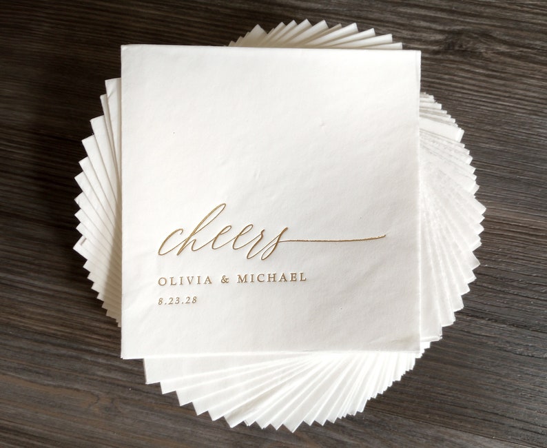 Gold Foil Wedding Napkins -Stack of personalized wedding napkins that say "Cheers" and are personalized with the couple's names and wedding date.