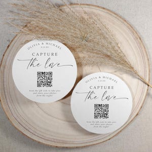 May include: Two white round cards with black text that reads "Olivia & Michael" and "Capture the love". Each card has a black and white QR code and instructions to scan the code to take pictures and share them from the night.