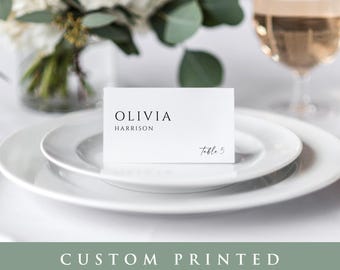 May include: White place card with black text reading "Olivia Harrison, Table 5".