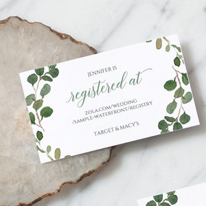 May include: A white card with green foliage border and the text "JENNIFER IS registered at ZOLA.COM/WEDDING /SAMPLE-WATERFRONT/REGISTRY TARGET & MACY'S"