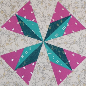 May include: A quilt block with a starburst design. The block is made of pink and teal fabric with a white background.