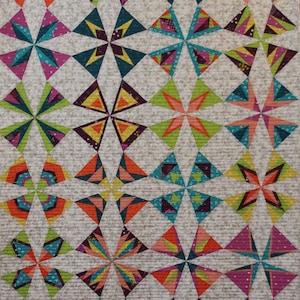 May include: A colorful quilt with a repeating geometric pattern. The design features starburst shapes composed of triangles in shades of teal, orange, pink, green, and yellow. The background is a light beige with a subtle floral pattern.