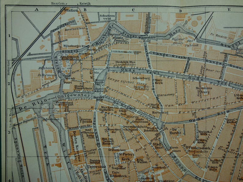 May include: A vintage map of a city, featuring a network of streets, canals, and buildings. The map is in shades of tan and brown, with black lines delineating the streets and waterways. Text labels identify landmarks and areas.