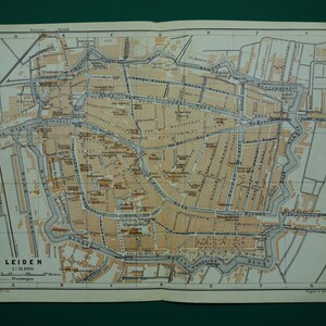 May include: A vintage map of Leiden, Netherlands, featuring a detailed street layout with canals and buildings. The map is printed in sepia tones with black and gray details. The title "LEIDEN" is visible at the bottom, along with a scale of 1:11,000.