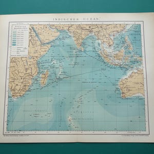 Pode incluir: Um mapa de papel antigo intitulado INDISCHER OZEAN mostrando o Oceano Índico, as costas da África, Ásia e Austrália em bege, e as profundezas do oceano em tons de azul. Inclui uma legenda, linhas de grade e rotas de navegação marítima.