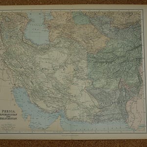 Op de afbeelding: Een antieke kaart van Perzië, Afghanistan en Beloetsjistan, met gedetailleerde geografische kenmerken. De kaart is gedrukt op verouderd papier, met tekst linksonder. De kaart toont de topografie van de regio, inclusief bergen, rivieren en kustlijnen.