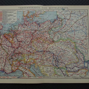 以下が含まれることがあります： 「Verkehrskarte von Mitteleuropa」（中央ヨーロッパ交通地図）と題されたヴィンテージ地図。中央ヨーロッパの道路や地理的特徴が詳細に描かれており、さまざまな色がルートを示しています。古紙に印刷されています。