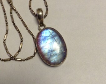 May include: A silver chain necklace with an oval-shaped pendant featuring a blue and purple iridescent gemstone.