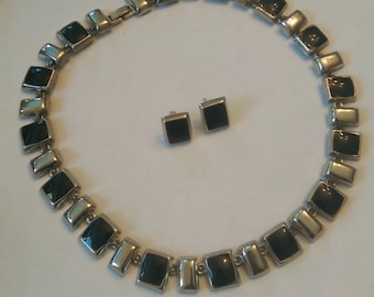 May include: A silver-toned necklace and matching square stud earrings. The necklace and earrings feature black square insets. The necklace is composed of rectangular and square links.