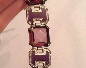 May include: A silver bracelet with a series of square-shaped purple glass stones set in silver frames. The bracelet has a hinged clasp.