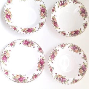 May include: Four white ceramic bowls with a floral rose pattern in shades of pink, peach, and green. The bowls have a scalloped edge and a silver trim. The bowls are arranged on a white surface.