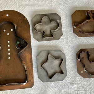 Op de afbeelding: Een verzameling vintage metalen koekjessnijders in verschillende vormen, waaronder een peperkoekman, een ster, een klaver, een eend en een kip. De snijders zijn gemaakt van koper en staal, met zichtbare lasnaden.