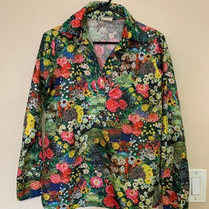 May include: A long-sleeved button-up shirt with a colorful floral print. The shirt has a dark green background with a variety of flowers in shades of pink, red, yellow, and blue.