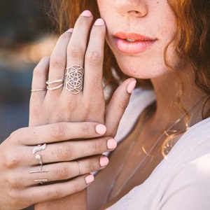 Puede incluir: Una mano de mujer con esmalte de u&ntilde;as rosa lleva varios anillos de plata, incluyendo un anillo de dise&ntilde;o geom&eacute;trico.