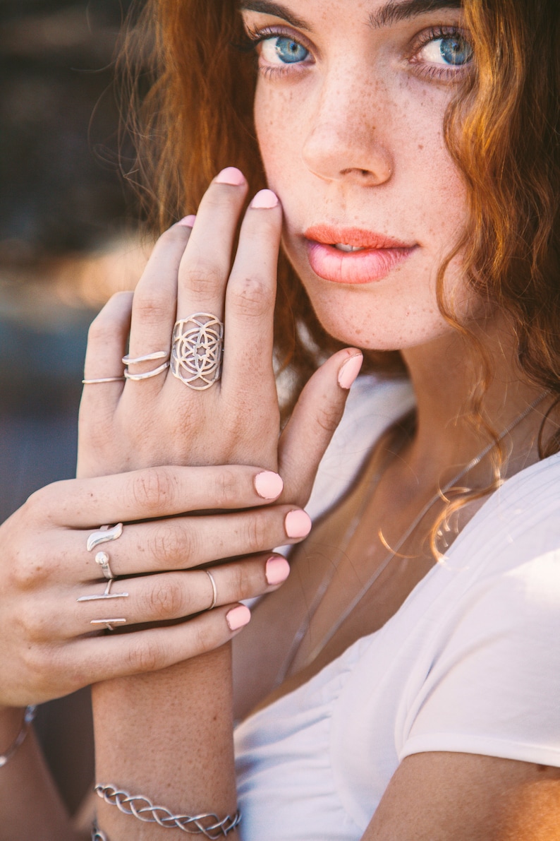 Puede incluir: Una mano de mujer con esmalte de u&ntilde;as rosa lleva varios anillos de plata, incluyendo un anillo de dise&ntilde;o geom&eacute;trico.