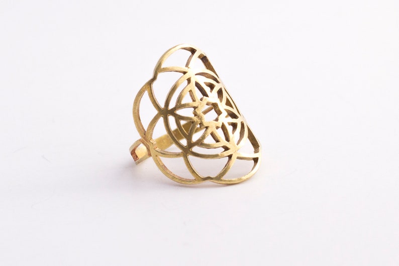 Puede incluir: Un anillo de color dorado con un dise&ntilde;o geom&eacute;trico. El anillo est&aacute; hecho de metal y tiene un patr&oacute;n delicado e intrincado.
