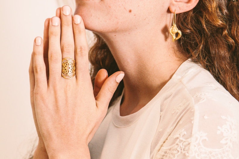 Puede incluir: Un anillo de oro con un dise&ntilde;o geom&eacute;trico. El anillo se lleva en el dedo &iacute;ndice de una mano.