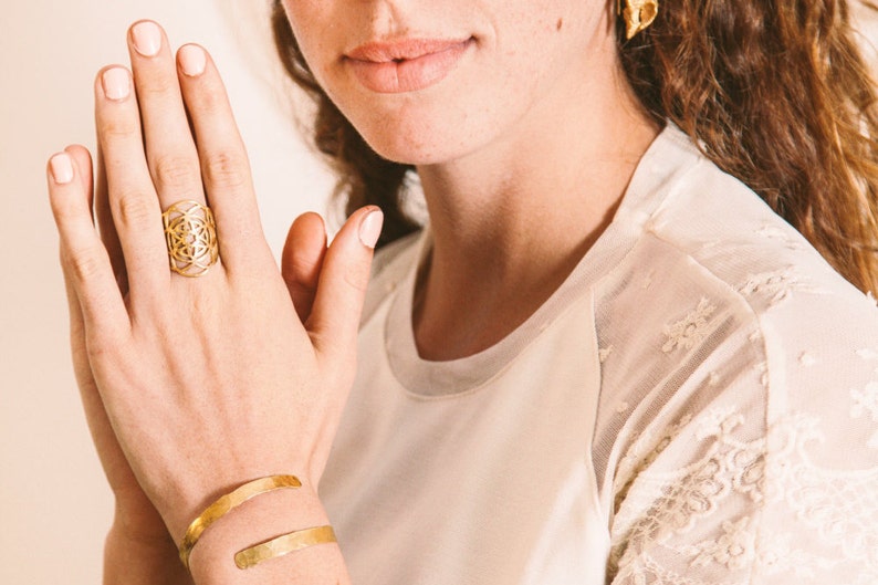 Puede incluir: Un anillo de oro con un dise&ntilde;o geom&eacute;trico. El anillo se lleva en el dedo &iacute;ndice de una mano.