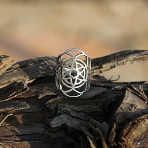 Puede incluir: Un anillo de plata con un dise&ntilde;o geom&eacute;trico, que recuerda a una flor o un mandala, sobre un fondo de madera.