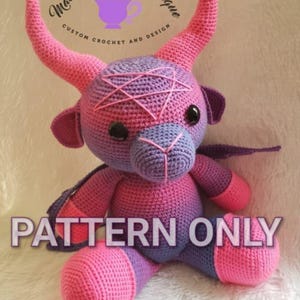 May include: A crocheted purple and pink bull with horns, a pentagram on its forehead, and the text "PATTERN ONLY" in large letters.