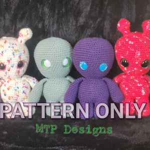 Puede incluir: Cuatro juguetes alienígenas de amigurumi tejidos a crochet en diferentes colores: blanco con motas multicolores, verde, morado y rosa con motas blancas. Los juguetes tienen ojos grandes y están dispuestos en fila. El texto "PATTERN ONLY" y "MTP Designs" es visible debajo de los juguetes.