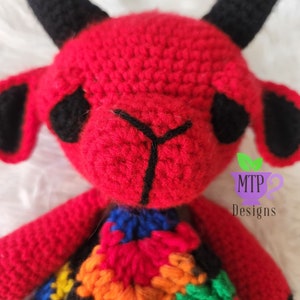 May include: A red crocheted devil with black horns and a colorful crocheted skirt. The devil has black eyes and a black stitched nose. The skirt is made of different colored squares. The image includes the text "MTP Designs".