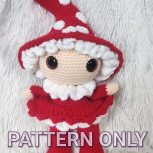 May include: A handmade crochet doll with a red mushroom cap with white spots, a red dress, and red boots. The doll has a beige face with large black eyes and a white ruffled collar. The text "PATTERN ONLY" is visible on the image.