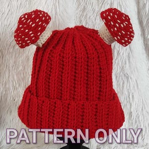 May include: A crochet pattern for a red beanie with two white and red mushroom accents. The pattern is called "PATTERN ONLY" and is by "MTP Designs".