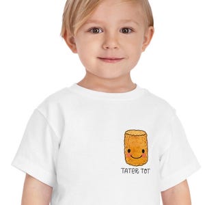 May include: White toddler t-shirt with a cartoon tater tot with a smiling face and the text "Tater Tot" underneath.