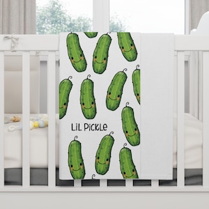 May include: White baby blanket with a green pickle pattern and the text "Lil Pickle".