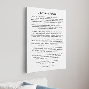 May include: A white canvas print with the text "A Father's Prayer" in black. The print is displayed on a wall above a white sofa with blue cushions. The text is a poem by General Douglas MacArthur.