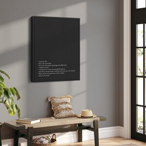 May include: Black and white typography art print with a quote about fear. The print is framed in a black frame and hanging on a gray wall above a wooden bench.