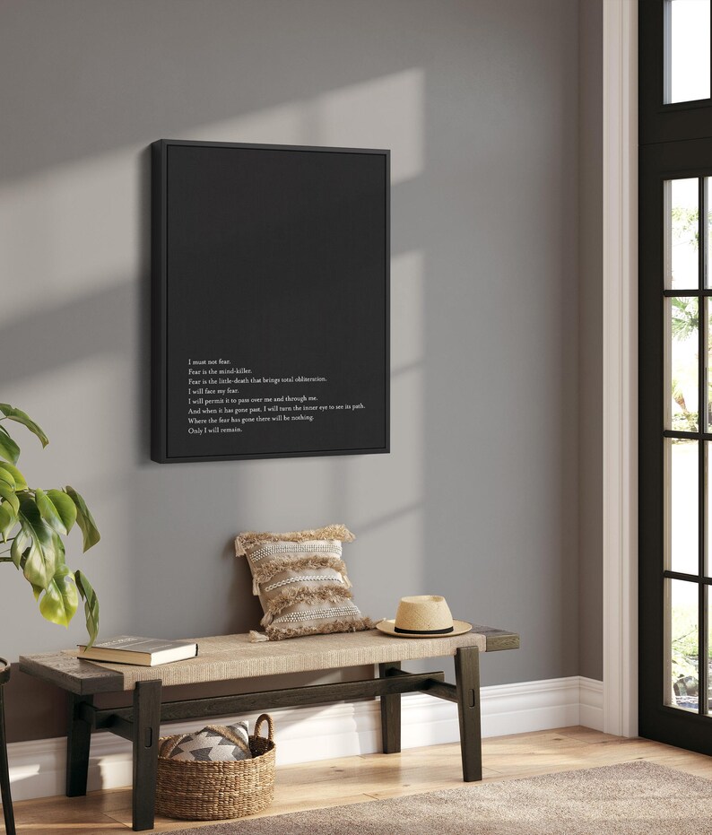 May include: Black and white typography art print with a quote about fear. The print is framed in a black frame and hanging on a gray wall above a wooden bench.